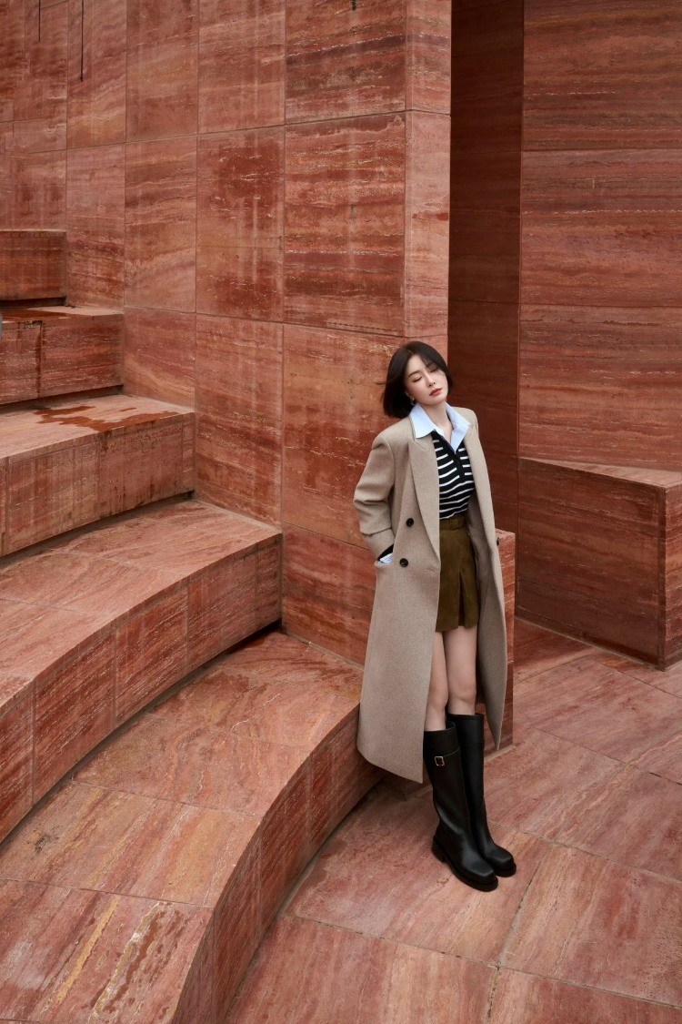 秦嵐這套 Look 完全示範了 40＋女生最值得照著穿的 「長外套＋短下身」減齡公式。長版駝色大衣本身帶著成熟與高級的氣場，但一換上短裙，立刻把整體視覺「減重」，內搭選擇條紋針織外套，黑色長靴拉出鮮明的上下比例，不僅顯腿長，也讓駝色大衣的優雅感更突出。