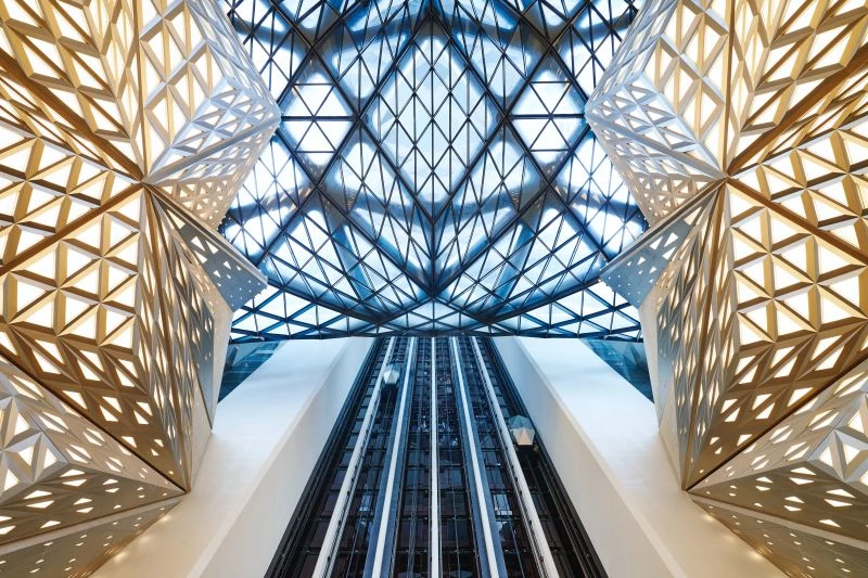 摩珀斯承襲建築大師 Zaha Hadid 的設計美學，將兩棟飯店主量體透過流動曲線相互連結，弱化視覺厚重感。清透的幾何玻璃帷幕，藉由白色鋼構的柔和包裹，賦予建築詩意與張力。40 米挑高的大廳與寬敞跨距成為光影變化的核心舞台。完工後，摩珀斯成為澳門重量級新地標。放眼亞洲，Zaha Hadid 團隊亦在台灣打造「淡江大橋」，在香港設計「The Henderson」商辦大樓，展現建築未來感與雕塑語彙。