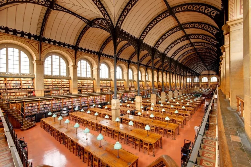 坐落於法國巴黎萬神殿(Panthéon)對面,聖熱納維耶芙圖書館(Sainte-Geneviève Library),是 19 世紀創新建築的代表作之一。館內雙拱形屋頂由細長的鑄鐵柱支撐,天花板上的格狀金屬結構為整體增添一抹精緻美感,在宏偉中展現優雅。這座圖書館不僅外觀典雅,內涵同樣深厚,其館藏源於 6 世紀的聖熱納維耶芙修道院,是一座極具歷史價值的文化遺產。