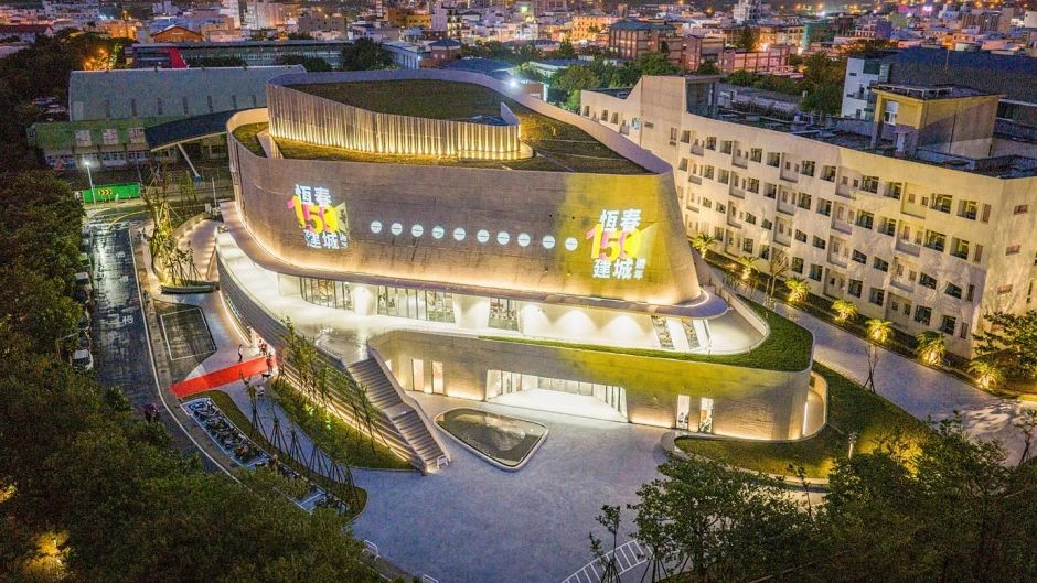 誠品書店恆春限定店的一大亮點,莫過於其建築空間設計。相較於過去偏向商業空間的選址脈絡,這回選在文化中心,也嘗試弱化其商業性。基地坐落於恆春古城東門旁,以「文化港灣」為概念,宛如停泊於海灣的船型建築,承載恆春半島的故事,邀請市民走入其中,打造靜謐的閱讀空間。