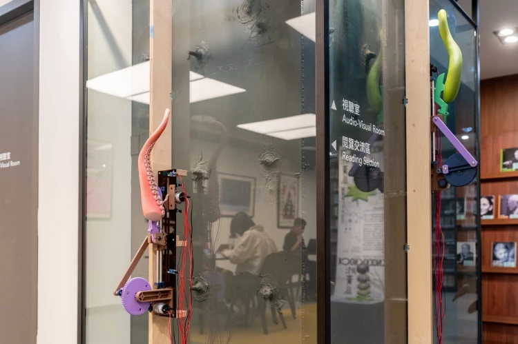 展覽《KnockKnock#1_ 黃瓜》是一場由五組動力裝置構成的空間演出。藝術家羅智信以圖書館內部的透明玻璃牆為創作起點。這道玻璃牆讓觀眾得以望見原本隱藏於建築體後的鋼構立柱,卻也形成一種「看得見卻無法接近」的感知經