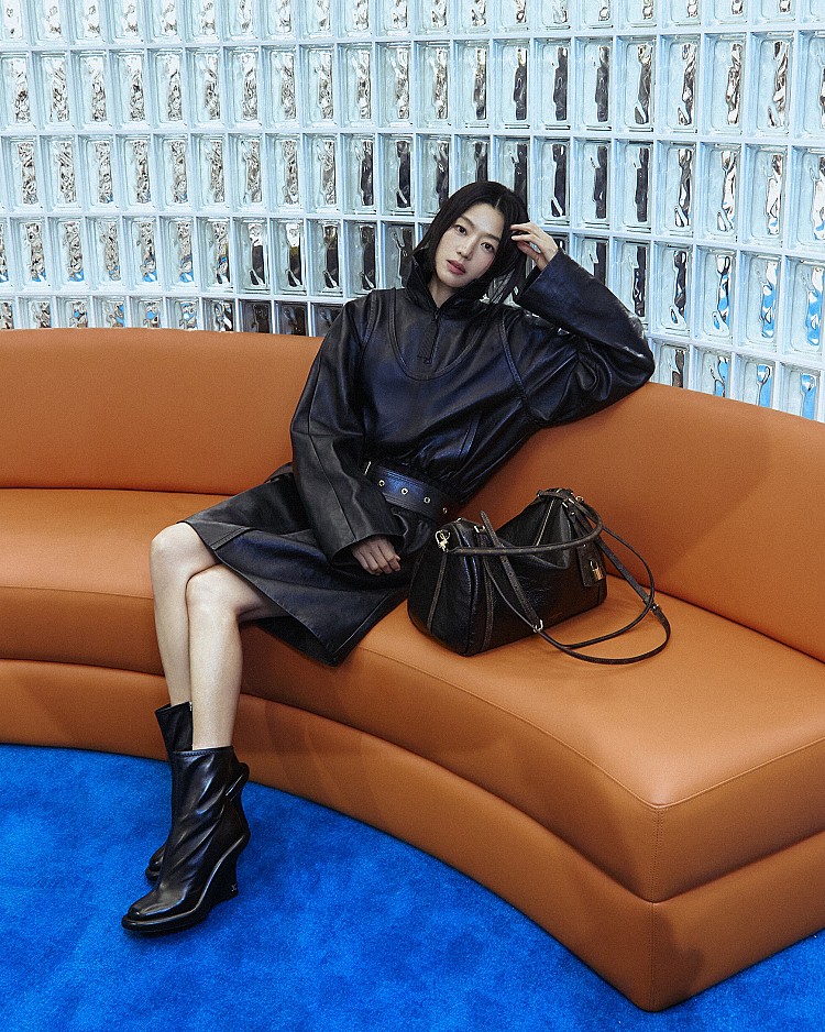 以一身率性的黑色皮革洋裝搭配短靴，上寬下窄的服裝線條，寬版皮帶的點綴，散發出冷豔俐落的高級感，而她一旁的 Louis Vuitton全新Express包款，是造型的點睛之筆，由Speedy包款再變身，並融入Keepall的經典元素，全智賢藉由皮革穿搭疊加此包款，優雅之中注入了年輕活力。