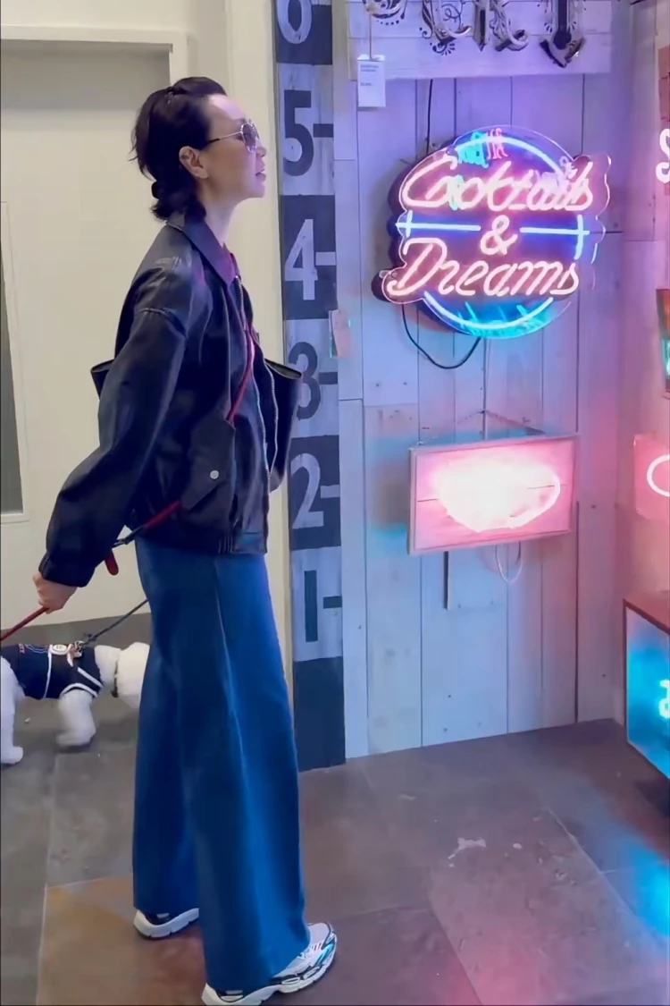 張曼玉牽著愛犬隨性逛街的這套造型，以一件版型挺拔的黑色皮衣穿搭打造俐落輪廓，她肩線與光澤感替整體增添一點「酷女孩」氣場，下身搭配高腰寬版牛仔褲，垂墜線條不只修飾腿型，也讓身形比例看起來更輕盈。最吸睛的是她手上揹的Gucci托特大包，容量大、造型簡潔，穿出減齡的「張曼玉式隨性」。
