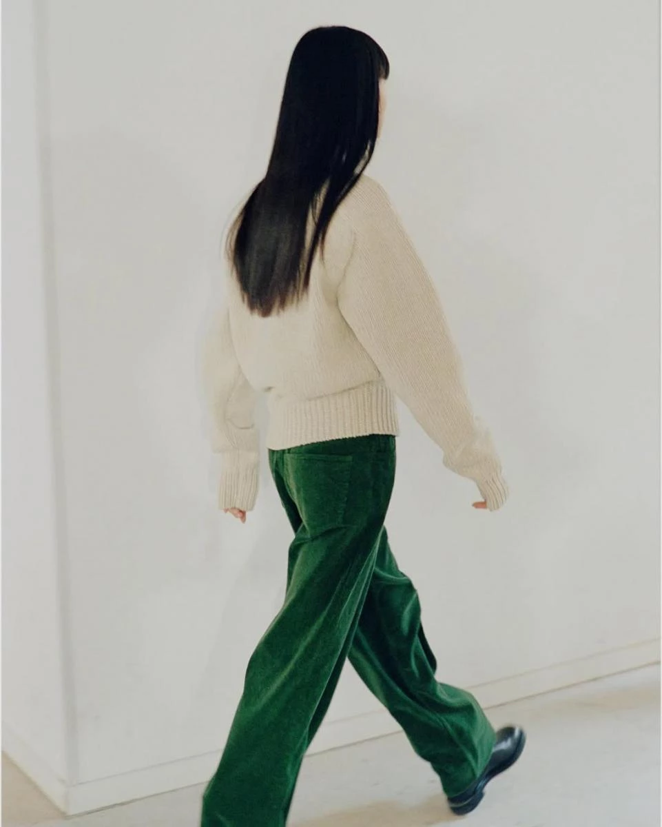 白色毛衣，綠色褲子的長髮女生。