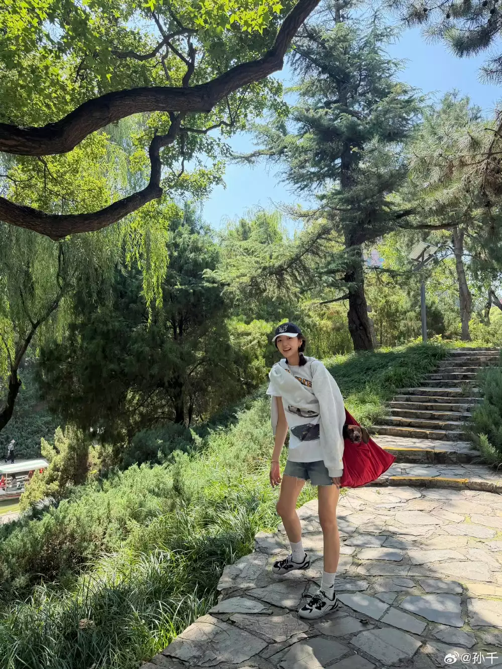 先看這套元氣滿滿的公園遛狗造型。孫千以一件Celine白色印花衛衣搭配水洗牛仔短褲,戴上深色棒球帽、背著紅色寵物背袋,青春又日常。腳上則是黑白配色的老爹鞋,厚實的鞋底與俐落的黑白撞色,替一身淺色調收出重心,再配上一小截白襪露出腳踝,視覺上把小腿線條拉得更修長。「上寬鬆、下短褲」的比例本身就顯腿長,再讓球鞋當作壓陣,整體輕鬆又高挑。