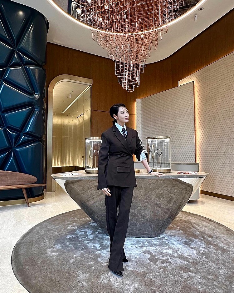 出席江詩丹頓腕錶活動時，金憓秀以一身深棕色西裝套裝亮相，款式上選擇在肩線鋒利、腰部收出精準線條，她特意將一邊袖口隨性捲起，讓整體造型在幹練之外更添率性與個性，巧妙削弱了正式感，下身則以微喇叭長褲修飾比例，搭配尖頭鞋，讓她的逆天長腿更加筆直修長。