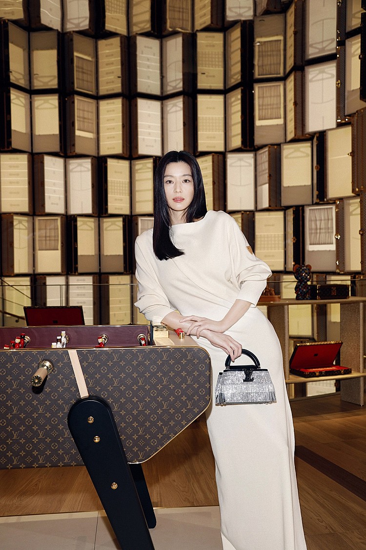 這套造型以奶油白色長洋裝打造極簡高級感，修長的剪裁線條在視覺上延伸比例，船型領的設計展露出剛剛好的性感，延續一貫的乾淨俐落，點綴上銀色亮片與黑色皮革拼接的經典Capucines包款，讓整體氛圍既優雅又不失時髦感。