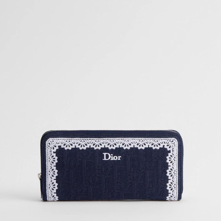 Dior Oblique Voyageur全新薄款長夾以深藍色Dior Oblique緹花為主體，搭配白色蕾絲邊框與刺繡標誌，拉鍊式設計讓內部收納一目了然，能平整放置鈔票與日常必需品。