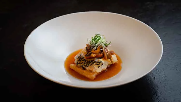 「古法蒸龍躉石斑」以豬油輕醃、豬網包裹蒸製,搭配五花肉片與醬油汁,鮮香滑嫩、香氣交融。
