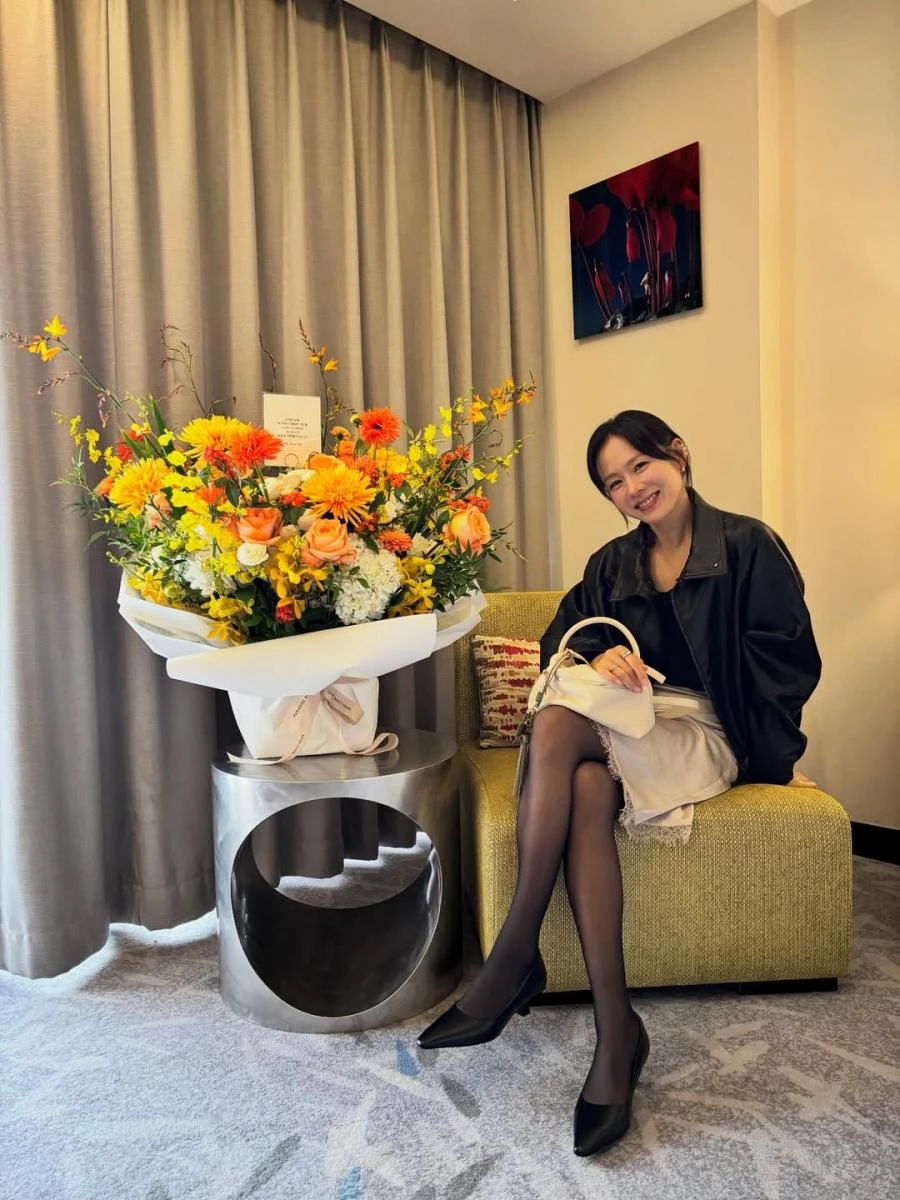 皮外套本身帶有率性與成熟氣場，若拿捏不當，容易顯得過於強勢。孫藝珍巧妙以絲綢質地的半身裙中和皮革的銳利感，透過光澤與垂墜感替造型注入柔軟層次，再搭配絲襪與尖頭小貓跟鞋，在剛與柔之間取得恰到好處的平衡，同時拉長腿部線條，使比例更顯修長。最後，手上那一只來自義大利品牌 testoni 的米色皮革包袋，搭配綠色幸運草吊飾，為整體加上一筆低調亮點，讓造型更顯質感，散發出沉穩卻不顯年紀的優雅氣質，非常適合輕熟女作為日常或正式場合的穿搭範本。