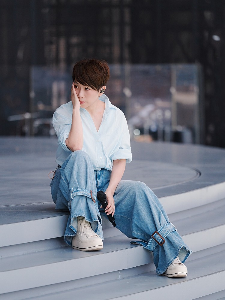 近日的造型中，林憶蓮以Oversize淺藍襯衫搭配有著綁帶設計的牛仔寬褲，加入金屬扣件與綁帶細節，結合街頭與音樂風格，腳踩白色厚底球鞋，為整體造型休閒感加分，同時展現隨性不羈的一面。
