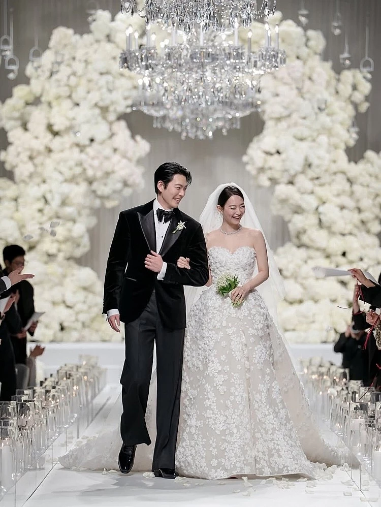 申敏兒主婚紗來自 Elie Saab 2026春夏新娘系列，定價約2萬8600美元，換算約 4200萬韓元、近新台幣98萬元。整件禮服以心型的剪裁展露出鎖骨線條，立體的花卉刺繡點綴，並適當的留白結合蕾絲細節，將頭髮簡單乾淨盤起，僅以Louis Vuitton白金鑲鑽Galaxie項鍊點綴，彷彿是仙女走入凡間。
