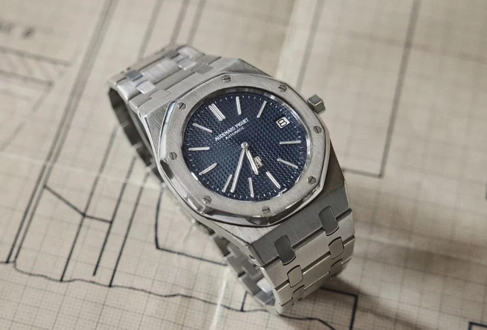 Royal Oak 的經典除了八角形框架,另一個無法忽略的核心,就是錶盤上那片猶如光影棋盤般的 Tapisserie 格紋。這不是印刷效果,而是以傳統 Guilloché 機刻工法雕刻而成,每一顆立體方格都有細微深淺差異,像微風掠過的海面,折射出近與遠、亮與暗的細緻層次。Felix 佩戴的皇家橡樹自動上鍊計時碼錶,採用 「Grande Tapisserie」大型格紋,色調採用最具歷史象徵的「雲夜藍50」,向1972年初代致敬。當玫瑰金指針在這片藍中移動,畫面像日落灑在海平面上,冷暖並存的色溫,讓整只錶既理性又感性。這種不追求大量複製、保留手工痕跡的雕刻語言,也使每一枚皇家橡樹都帶著微不可見的獨特性,並成為能被「一眼認出」的存在。