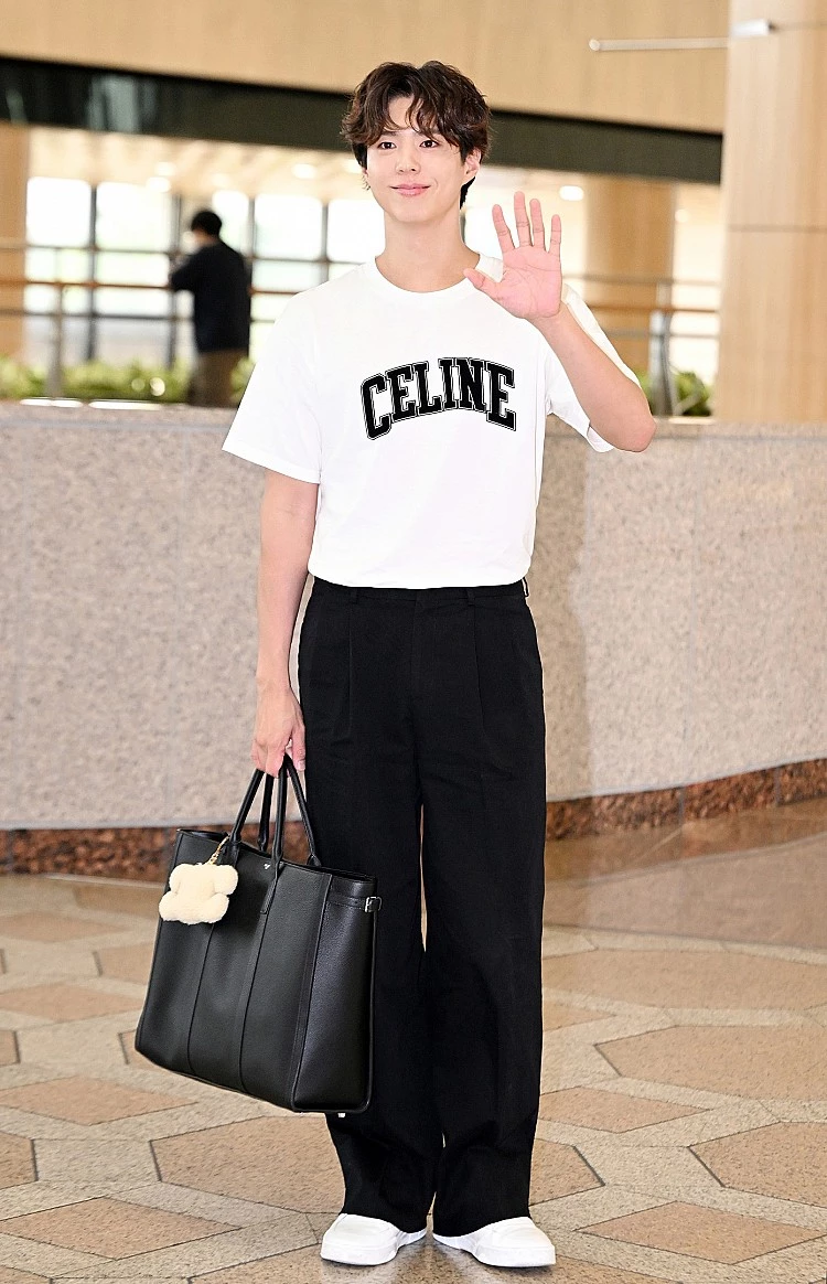 朴寶劍他選擇Celine白色Logo T恤搭配黑色西裝寬褲，簡單俐落卻不失高級感，手中拎著大型黑色公事包，並掛上毛絨吊飾，讓整體造型多了點俏皮細節。白色球鞋呼應T恤色調，營造出夏日輕盈氛圍，非常適合機場穿搭。