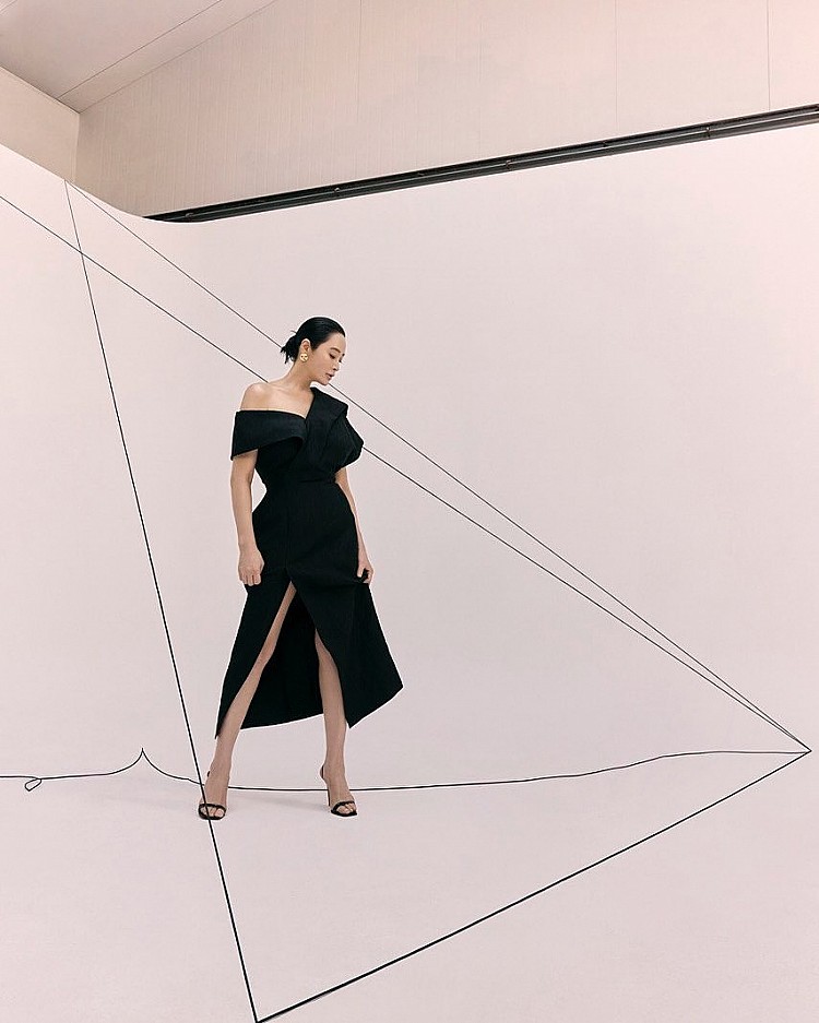 金憓秀以一襲不對稱風衣式黑色洋裝，立體剪裁巧妙修飾肩膀與腰線，開衩設計延伸腿部線條，腳踩著細帶高跟涼鞋，極簡之中有著恰到好處的性感，營造出「剛柔並濟」的視覺平衡。