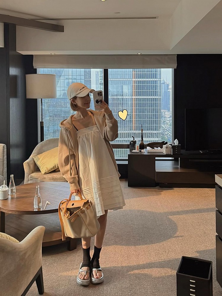 常在室外、室內奔走的女孩們，請參考這一套穿搭！她以一件米白色寬鬆洋裝為主角，搭配同色系米膚色連帽外套，不僅層次柔和，也是在冷氣房中保持溫度與氣質的完美解法，配件上選擇Hermès Herbag帆布皮革包，呼應整體穿搭中的奶油色調，是個清新慵懶的搭配。