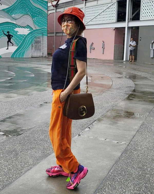 漫步在戶外園區,藍心湄以深色短袖T恤搭配亮橘色運動休閒褲,頭戴橘色漁夫帽,腳踩桃紅撞色運動鞋,斜揹經典品牌包款。整套Outfit兼具戶外活動的舒適度與滿滿的潮流感。休閒運動風,是減齡效果最好的風格之一!日常運動或出遊時,試著把黑灰色運動褲換成飽和度高的亮色系(如橘色、寶藍色),再搭配一頂修飾臉型的漁夫帽,立刻精神抖擻。