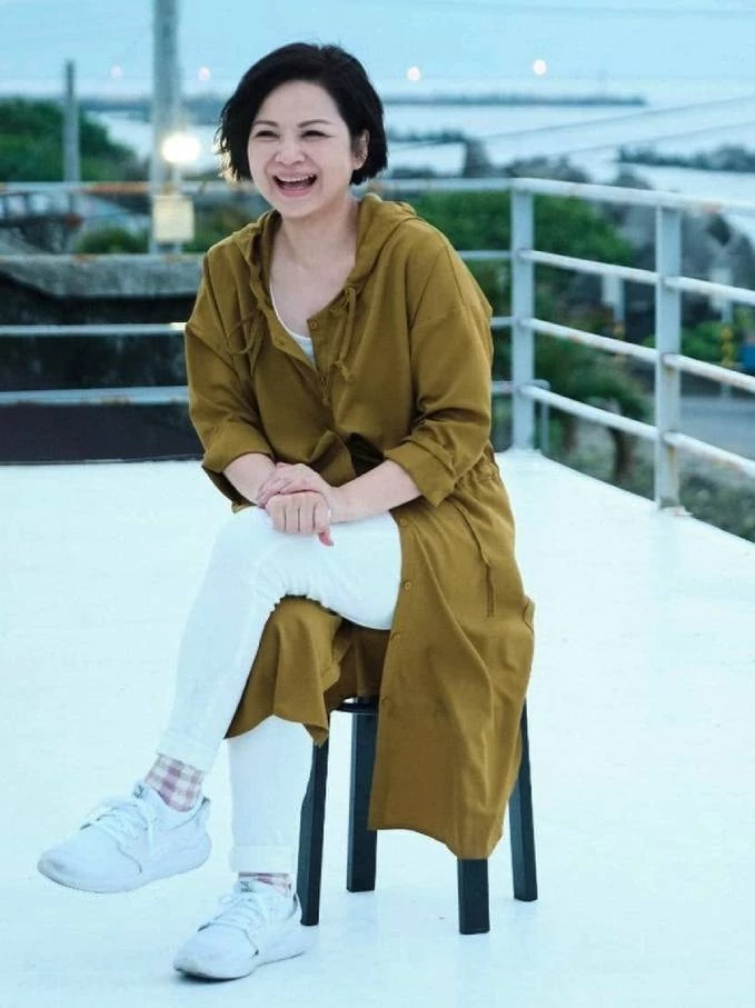 迎著海風、坐在凳子上笑得燦爛的楊貴媚,這套橄欖綠的連帽長版罩衫,搭配白色緊身褲與小白鞋,展現出極佳的休閒混搭功力。特別是那雙帶有格紋的小襪子點綴,簡直是細節滿分!整個人散發出隨性、熱愛生活的自在氛圍,讓人忍不住想跟著一起旅行。喜歡戶外活動或舒適穿搭的同齡人,建議可以選擇長版罩衫或風衣來修飾臀部與大腿線條,內搭清爽的白色褲裝,再踩上一雙好走的休閒鞋,既遮肉又顯高,舒適與時髦兼得。