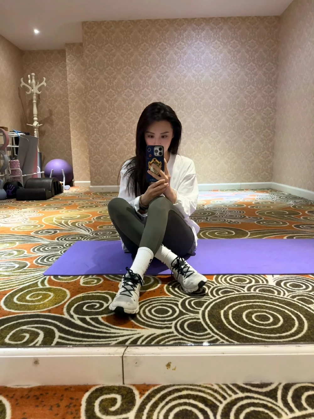 40歲毛林林以寬鬆白襯衫搭配灰綠色緊身內搭褲與白襪,腳踩On昂跑白色小白鞋(黑色鞋帶),在瑜珈室對鏡自拍,運動休閒又減齡。