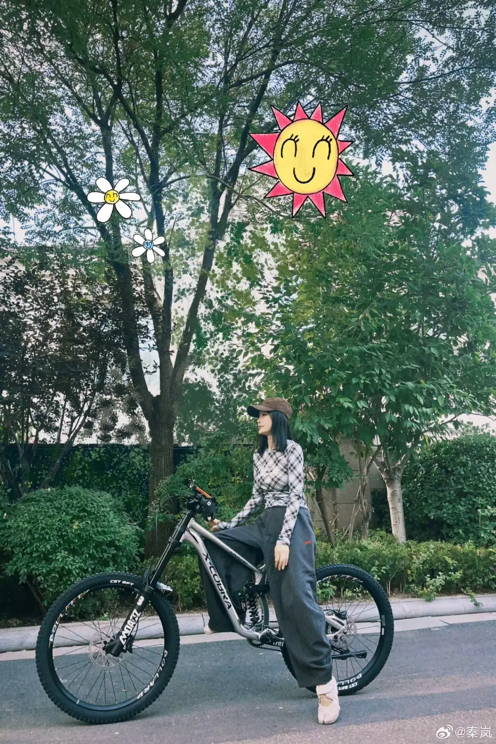 47歲秦嵐以黑白格紋合身長袖上衣搭配灰色垂墜運動寬褲,戴棒球帽、腳踩白色運動鞋,靠在腳踏車旁,率性又減齡。