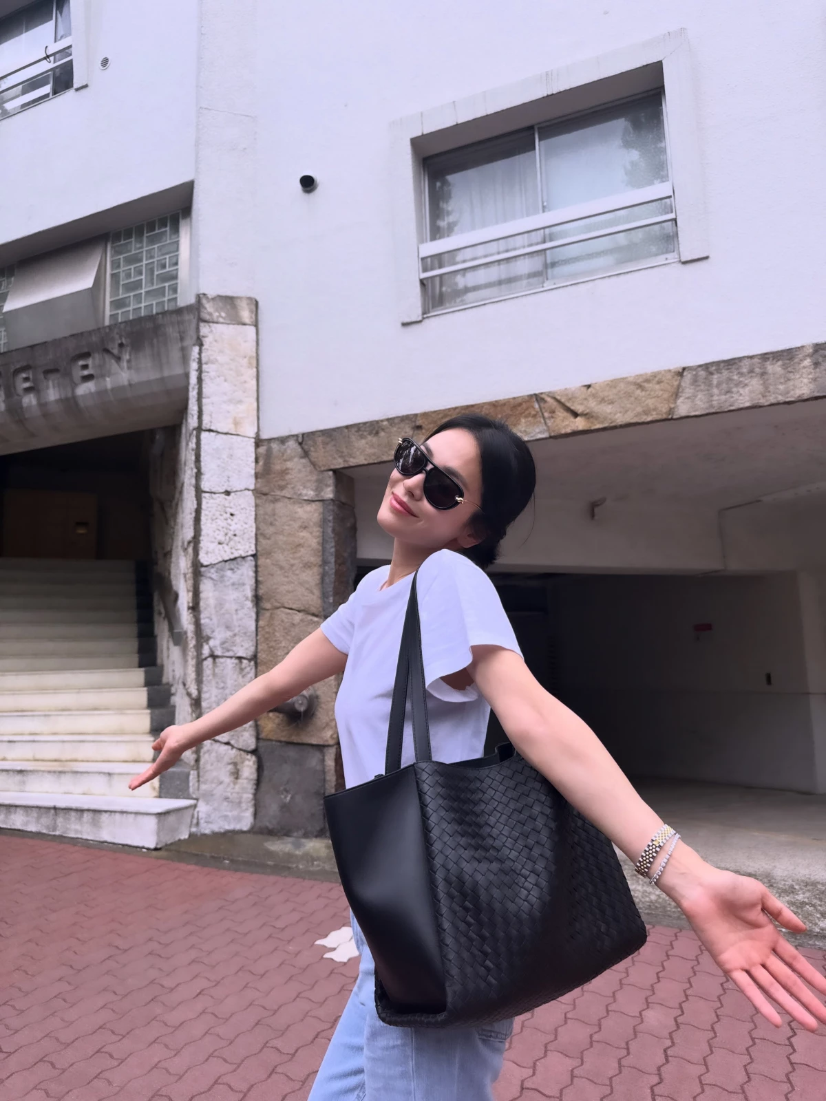宋慧喬以一件白色V領T恤搭配淺色牛仔褲，腳踩白色小白鞋、配上一截白色短襪，再拿一只Bottega Veneta黑色編織托特包與墨鏡點綴