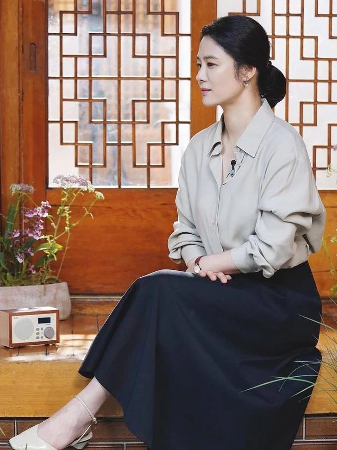 金賢珠坐在傳統木格窗前的這套穿搭,散發出滿滿的「靜奢風」質感。帶有一點灰綠調的柔順襯衫,搭配深藍色長裙與白色繞踝低跟鞋,整體色彩低調內斂,卻把她身上那種沉靜、優雅的書卷氣襯托得淋漓盡致。