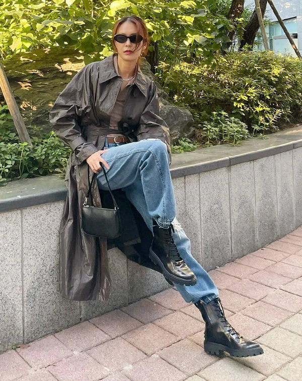 鄭釉珍身穿光澤感的深褐色中長版風衣，內搭貼身大地色上衣，下身大膽混搭刷舊高腰牛仔褲與厚底軍靴，臉上一副黑色墨鏡點綴。這套完美示範了如何把日常基本款穿出強大氣場，率性中帶著一絲不羈。