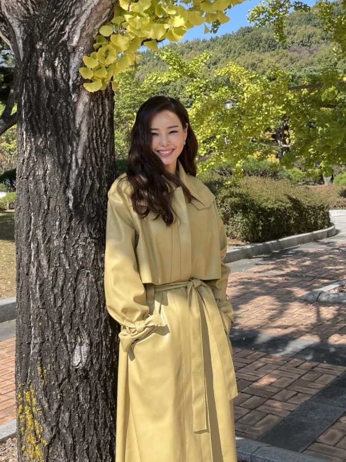 皮革風衣，往往容易給人沉重或過於銳利的霸氣感，但李荷妮聰明地挑選了帶著淡淡奶油黃的皮革材質。在陽光與銀杏樹下，這種柔和的淺亮色調能自然為肌膚打上「嫩膚濾鏡」，既保留了風衣特有的率性俐落，又完全消解了熟齡感常見的嚴肅僵硬。