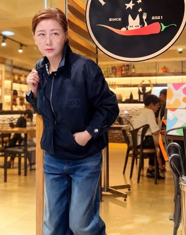 在餐廳門口,藍心湄身穿一件帶有經典雙C暗紋標誌的深藍色防風立領夾克,搭配深色高腰牛仔褲,展現出俐落又帥氣的都會風采。簡約的深色調沉穩有質感,而夾克的立領與修身剪裁則帶出神采奕奕的精神感。