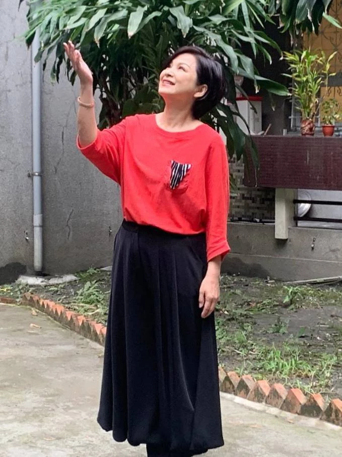 楊貴媚身穿搶眼的紅色上衣,搭配黑色長裙,沐浴在陽光下顯得神采奕奕,透出一股溫暖而充滿生命力的生活情調。 許多同齡人對大紅色有些卻步,其實,只要選擇帶有設計巧思(如撞色口袋、拼接剪裁)的紅色上衣,並搭配沉穩的黑色長裙或長褲來平衡視覺彩度,就能把紅色的熱情轉化為襯托好氣色的利器,穿出年輕朝氣卻不顯浮誇。