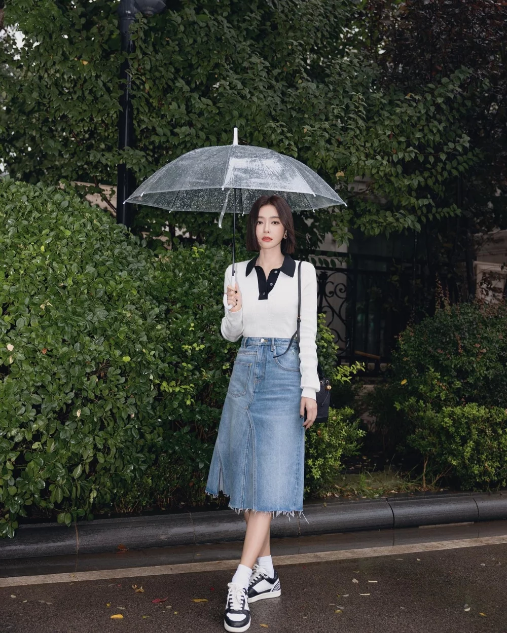 秦嵐雨天撐透明傘,以黑領白色Polo針織上衣搭配牛仔A字裙、白色短襪與Tory Burch黑白四葉草球鞋,學院風俐落又減齡。