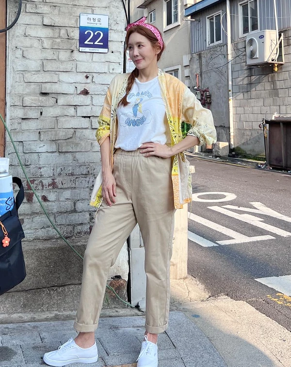 這套街頭私服充滿了童心與復古韻味！圖案印花T恤搭上黃色圖騰開襟外襯，下身選擇九分卡其褲與白色休閒鞋，最神來一筆的是頭上的粉紅圖騰髮帶與側編髮。豐富的印花與配件互相呼應，呈現出金廷恩一種隨性自在、隨時準備出遊的放鬆感。記得多多運用「髮帶」或「印花絲巾」作為造型配件喔，是熟齡女性展現俏皮感的絕佳小巧思，能迅速為平凡的休閒裝注入精緻度。