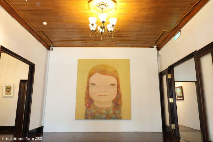 作為日本藝術家奈良美智的代表作之一,《朦朧潮濕的一天》靈感來自他在台灣旅行的經驗,同時傳遞對台灣在 311 東日本大地震期間的協助與關懷,以及疫情期間捐贈口罩的善意回應。他以更平靜、充滿餘裕的狀態完成這幅畫,畫中融入台灣居民的笑容、在地山巒疊嶂的群山等溫暖元素,透過小女孩的眼神,展現更多深層隱喻。