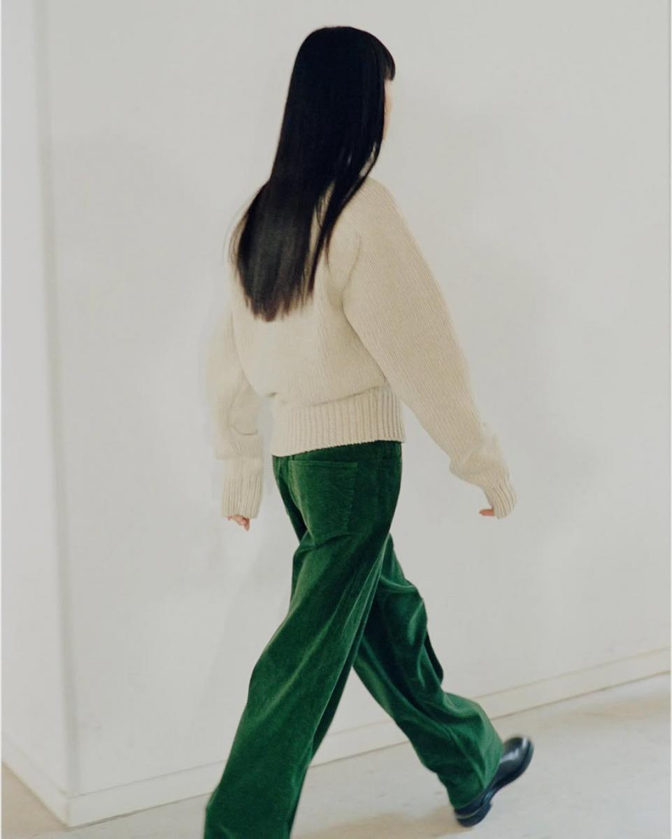 白色毛衣,綠色褲子的長髮女生。