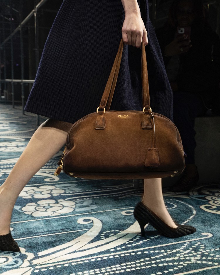 宛如一抹秋日濾鏡,這款保齡球包以溫潤麂皮勾勒出優雅的半圓輪廓,濃郁的棕色質地與細緻包邊形成對比。