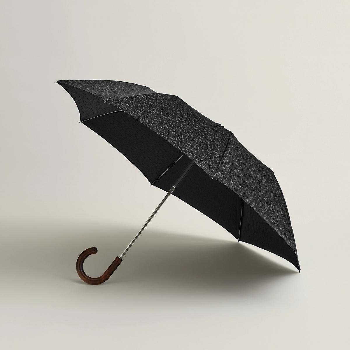 在雨天裡撐開這把 Pluie de H 折疊傘，彷彿走入一場 Hermès 的字母雨。黑色緹花帆布上，無數的 H 字母從天際傾瀉而下，呼應設計靈感「巴黎福寶大道的櫥窗漫步」。