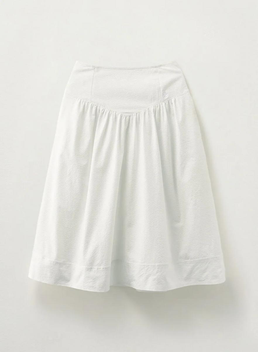 這件白裙是打造清爽造型的關鍵。立體布料帶有細微光澤，腰部 V 字拼接與均勻的褶皺設計，讓裙擺隨風搖曳時，充滿律動感。