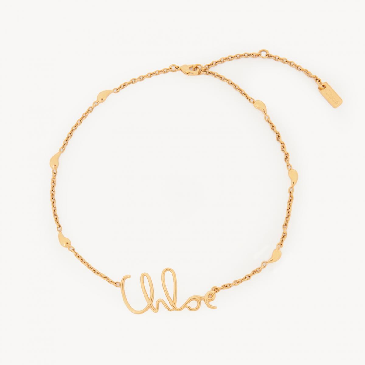 Chloé 的 Iconic Logo 項鍊，帶著一種溫柔卻堅定的力量。復古金色黃銅材質，靈感源自品牌典藏的鏈條腰帶，以柔美的手寫字體拼出「Chloé」字樣，像是佩戴者胸前的一份親密簽名。