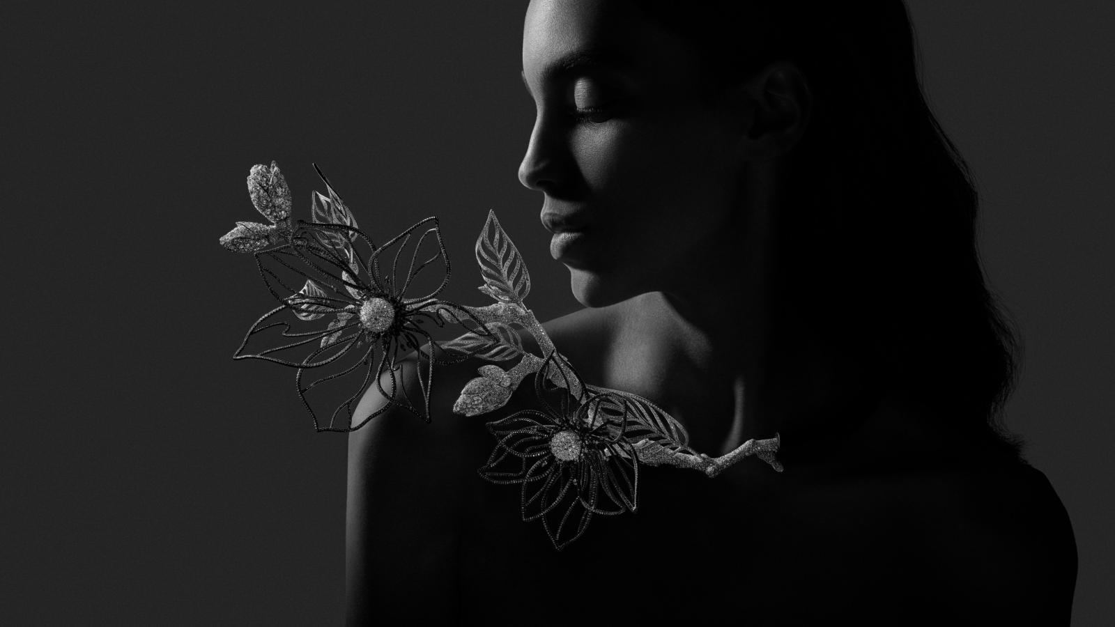 夜色未散，木蘭以殘影之姿橫向舒展，像是定格在空氣裡的最後一抹光。鋁材與黑陶瓷塗層塑造通透質感，花瓣上的倒鑲鑽石更讓光線逆向折射，呈現出意料之外的光芒。正如花道不僅著眼於花開的瞬間，而是整株植物的姿態，這裡的「間」不再只是空間，而是時間的停頓。同時，它也體現了侘寂哲學，在未竟與消逝之間，仍能看見一種深沉的優雅。枝間的竹節蟲以精緻姿態潛藏，提醒觀者即使是最微小的生命，也有屬於它的舞台。