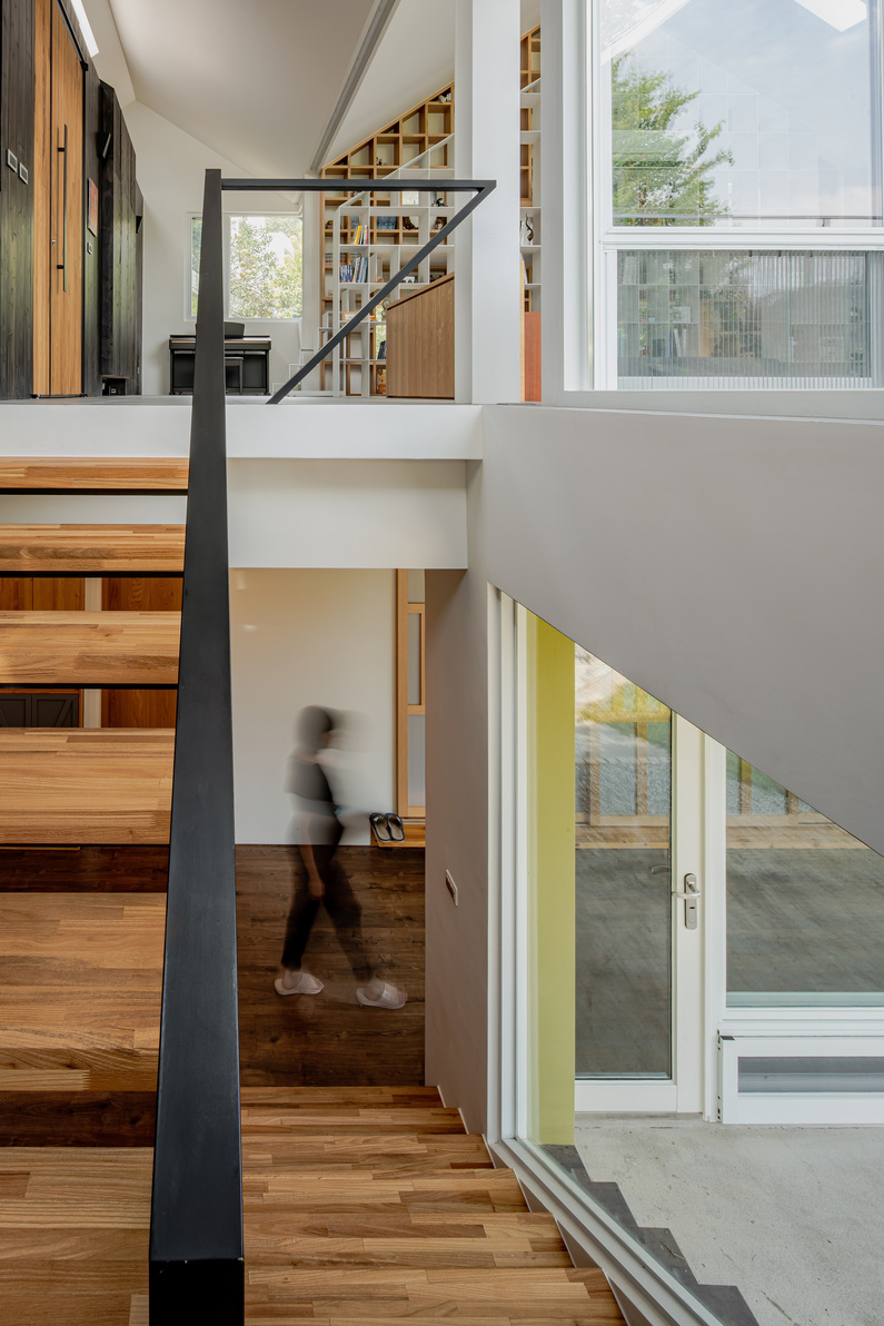 挑高的客廳空間，成為入室的一處驚喜。下沉式的地板設計形塑空間的層次性，同時也增加家人間的凝聚力。山簷屋頂下的空間同時也是開放、連續、流動的生活場，轉譯連綿山巒的語彙，彷彿置身於山脈之下。透過動線與家具的擺設，注入更多溫暖的情感氛圍。立面上，建築師也嘗試開了多扇幾何窗，透過大面積的玻璃及木格柵，堆砌出陰影的層次變化。