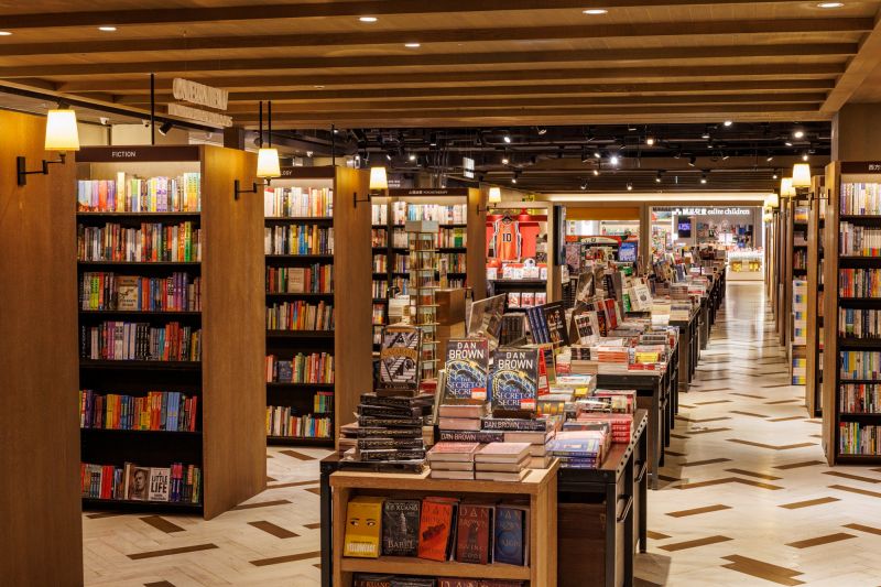 除了揉入誠品敦南店的「坐讀階梯」,松菸 24 小時書店也打造全新 40 米的閱讀長廊,重塑過往誠品信義店的寬敞書冊廊道,總書量更擴增 1 成,達到 25 萬冊。不僅藉由寬敞的走道形塑書店氛圍,也透過書架中島設計,讓閱讀者能自由地穿梭於書海中,結合書櫃排列與小檯燈,增添一抹溫度。