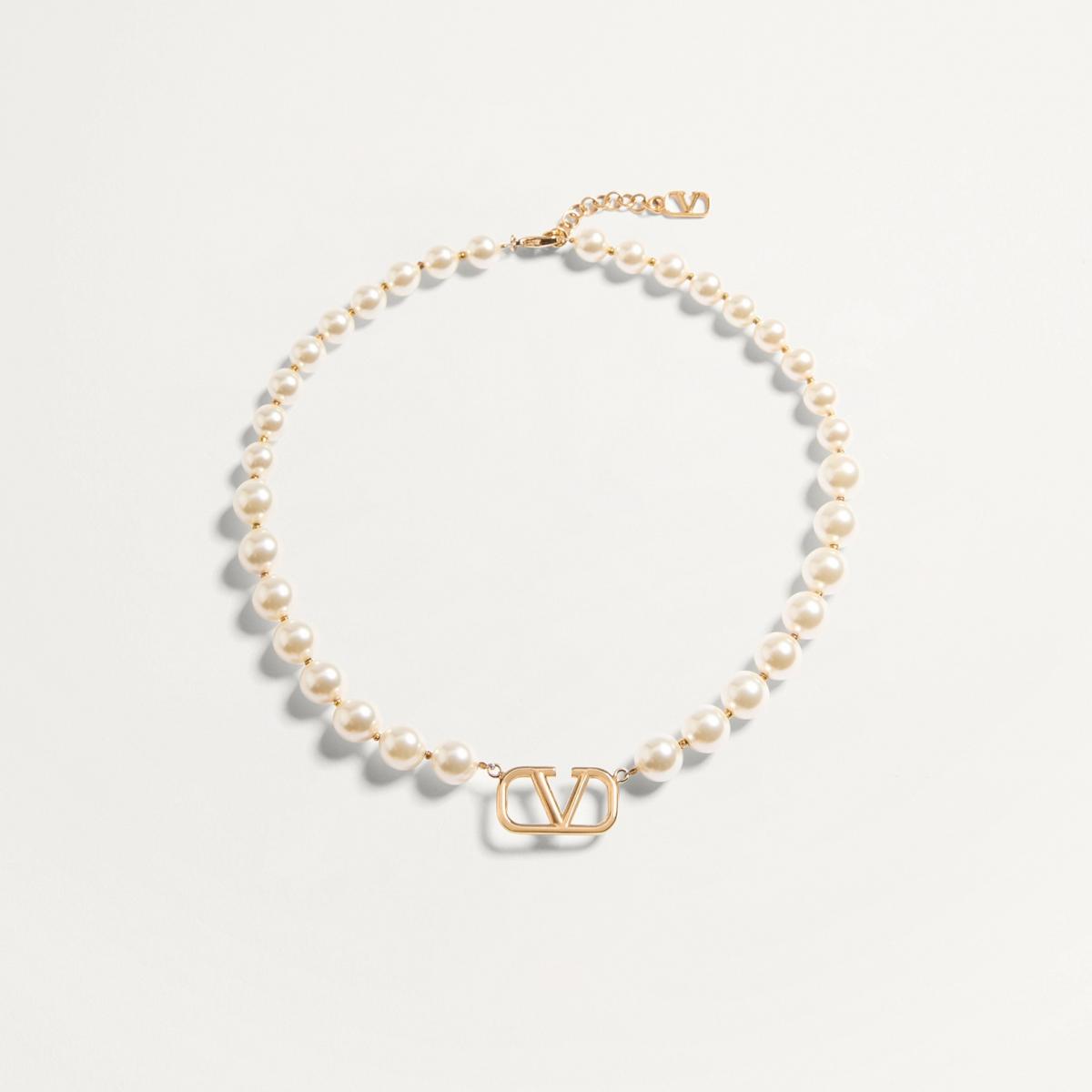 Valentino 的 VLogo Signature 項鍊以金色金屬搭配樹脂珍珠，中央的鏤空 V 字 Logo 簡約而醒目。它不像誇張的珠寶那樣搶戲，而是在不動聲色間散發精緻氣場。適合搭配白襯衫或羊毛針織，讓「簡約」成為最有力量的宣言，一如品牌一貫的羅馬優雅。