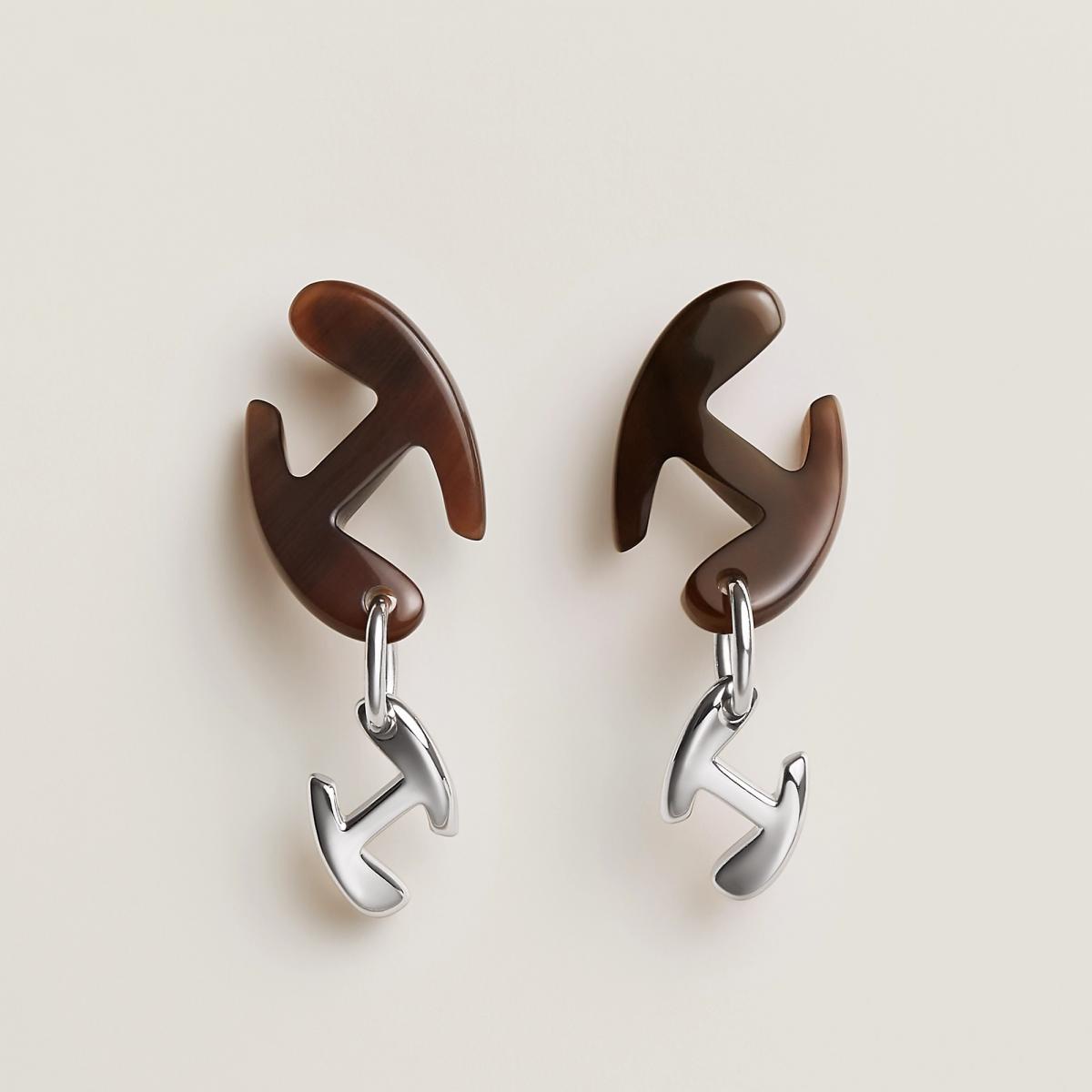 愛馬仕的經典從不止於皮革。這款 Chaine d’H 耳環靈感來自品牌馬具中的鍊條結構，將剛毅金屬與天然牛角結合，成就出一種「靜中帶勁」的美感。天然材質讓每一只耳環的紋理都獨一無二，如時間在質地上留下的筆觸。它不追求對稱的完美，反而以有機的不規則曲線，呼應現代女性自由不羈的姿態。