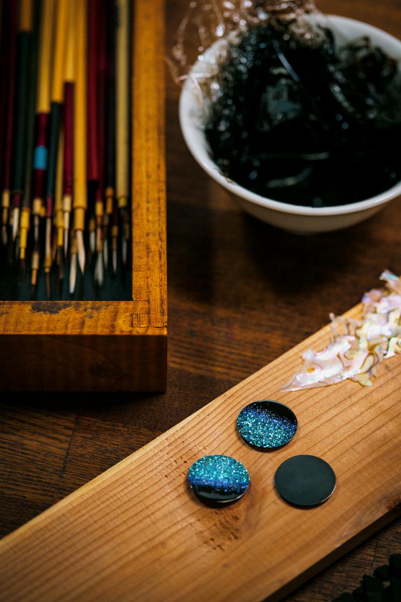 源自史前時代的漆藝（Urushi）向來被視為能承載靈魂的材質，以天然樹脂為基底，質地濃稠、色澤溫潤，靜謐得像一口能倒映宇宙的黑湖；而誕生於1300年前的螺鈿（Raden）則像往湖面撒下一把星屑，以細碎的珍珠母貝折射出光的萬種形貌，構成細膩且繁複的紋理，被譽為「會閃耀的繪畫」。在這次合作中，淺井康宏以兩項古老技法於 33mm 錶盤上打造一片凝縮夜空。珍珠母貝經大師精挑細選，每一片都在光下翻動、比較，彷彿是在找尋最適合落入夜色的星光；當它們被一一嵌入層疊漆面時，虹彩瞬間像深海與星夜交會般浮現。這是種不倚賴色塊，而是靠「光線本身」說故事的美。