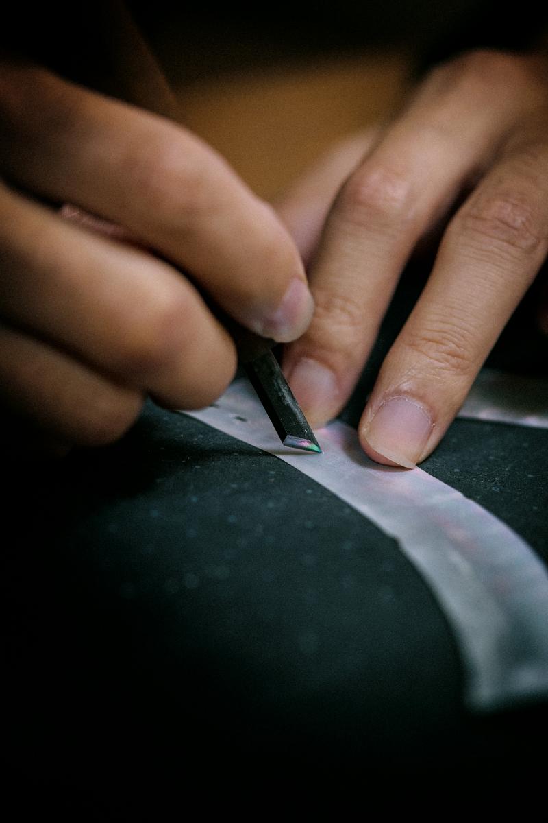 源自史前時代的漆藝（Urushi）向來被視為能承載靈魂的材質，以天然樹脂為基底，質地濃稠、色澤溫潤，靜謐得像一口能倒映宇宙的黑湖；而誕生於1300年前的螺鈿（Raden）則像往湖面撒下一把星屑，以細碎的珍珠母貝折射出光的萬種形貌，構成細膩且繁複的紋理，被譽為「會閃耀的繪畫」。在這次合作中，淺井康宏以兩項古老技法於 33mm 錶盤上打造一片凝縮夜空。珍珠母貝經大師精挑細選，每一片都在光下翻動、比較，彷彿是在找尋最適合落入夜色的星光；當它們被一一嵌入層疊漆面時，虹彩瞬間像深海與星夜交會般浮現。這是種不倚賴色塊，而是靠「光線本身」說故事的美。