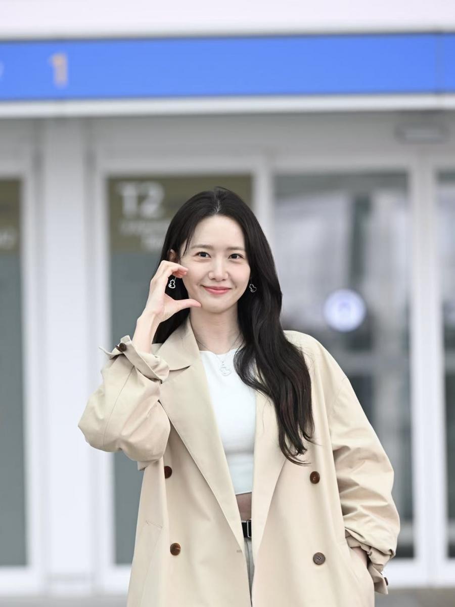 潤娥的機場穿搭選擇了經典米杏色風衣搭配白色短版上衣，乾淨、俐落、毫不費力。乍看是極簡的基本款組合，但真正的亮點落在耳畔及胸口的 Qeelin Wulu 18K白金鑽石及 Akoya 珍珠耳環及項鍊。珍珠的光澤如晨霧裡的第一滴露水，低調卻能瞬間點亮整體氣質。風衣偏中性的線條，透過珠寶柔和的曲線與光華，被轉化成更親切、更溫柔的氛圍。再加上 Wulu 象徵好運的寓意，使這套機場 Look 帶有「輕鬆出發、好事相隨」的明亮感。潤娥的穿搭非常高明，讓基本款風衣，也能靠一對質感珠寶，增添氣勢與完整度。