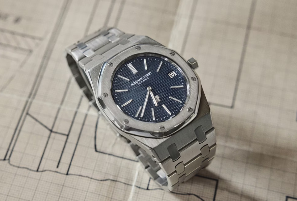 Royal Oak 的經典除了八角形框架，另一個無法忽略的核心，就是錶盤上那片猶如光影棋盤般的 Tapisserie 格紋。這不是印刷效果，而是以傳統 Guilloché 機刻工法雕刻而成，每一顆立體方格都有細微深淺差異，像微風掠過的海面，折射出近與遠、亮與暗的細緻層次。Felix 佩戴的皇家橡樹自動上鍊計時碼錶，採用 「Grande Tapisserie」大型格紋，色調採用最具歷史象徵的「雲夜藍50」，向1972年初代致敬。當玫瑰金指針在這片藍中移動，畫面像日落灑在海平面上，冷暖並存的色溫，讓整只錶既理性又感性。這種不追求大量複製、保留手工痕跡的雕刻語言，也使每一枚皇家橡樹都帶著微不可見的獨特性，並成為能被「一眼認出」的存在。