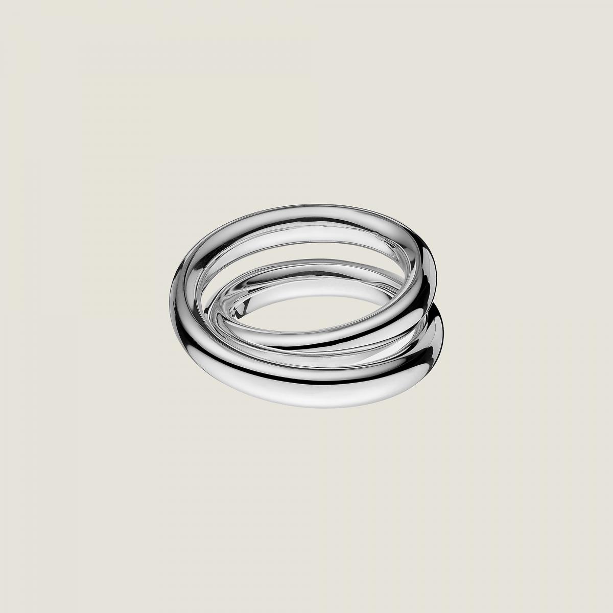 Vertige 戒指以流動線條包覆指節，彷彿金屬在空中旋轉後自然停留的瞬間。靈感源自 Double Tour 的設計概念，戒指並非單純環狀，而是以層層纏繞的姿態呈現，帶來視覺上的張力與節奏感。這種「未完全閉合」的結構，讓戒指在佩戴時顯得輕盈卻充滿動態，隨光線變化產生細膩反射。由 Martin Margiela 操刀的原創設計，讓 Vertige 成為 Hermès 珠寶中最具思想性的一款，低調卻極具辨識度。