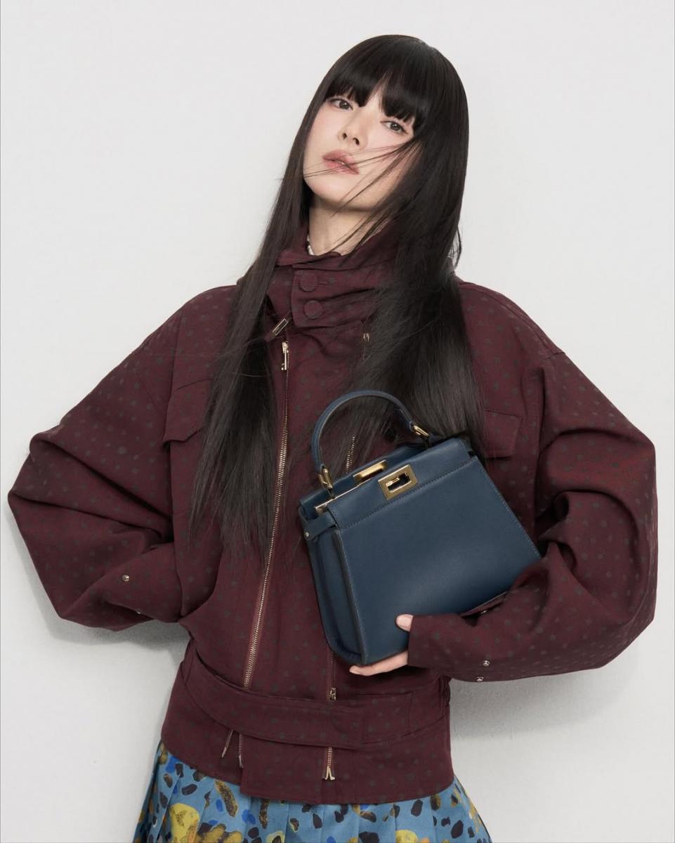 線條俐落的 Oversized 外套搭配印花百褶長裙，透過剛與柔的對比，讓造型在穩定中保有輕盈感。外套的結構感為整體定下成熟基調，而裙裝的圖紋與垂墜線條則柔化視覺，避免造型顯得過於嚴肅。宋慧喬刻意讓視覺亮點集中在下半身，使整體比例更顯修長，也讓穿搭多了一分流動感。這樣的組合不追求少女感，而是用層次與節奏創造減齡效果，是相當值得借鑑的搭配思路。