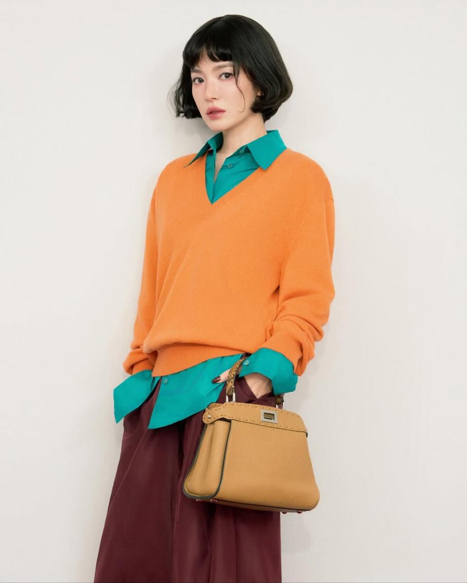 綠色襯衫疊搭橘色針織衫，透過暖冷色調的對比，讓造型層次自然浮現。橘色帶出活力，綠色則穩住視覺重心，使亮色不顯張揚；下身的酒紅長裙進一步拉長比例，也讓整體色彩過渡更加和諧。宋慧喬善用飽和但不刺眼的配色，營造出俏麗而克制的風格。這樣的色彩疊穿不追求吸睛效果，而是讓造型看起來有精神、有深度。